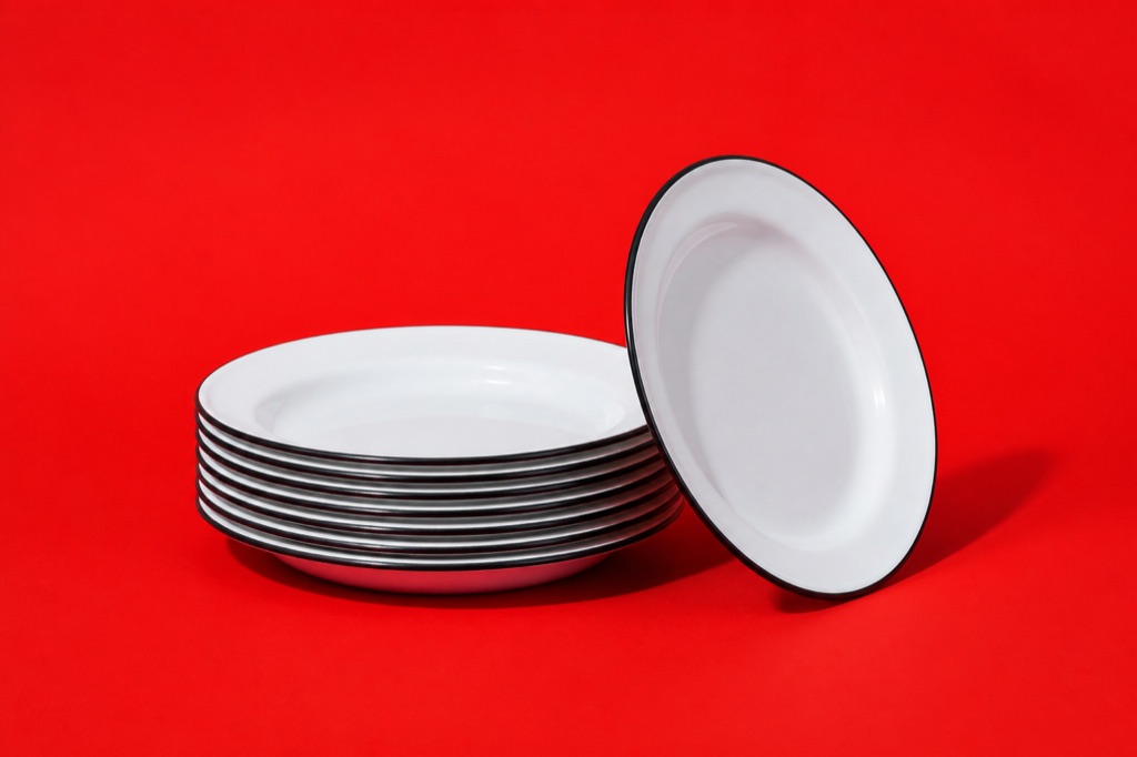 A stack of white enamel plates on a tomato-red backdrop, one plate stood on its edge against the stack