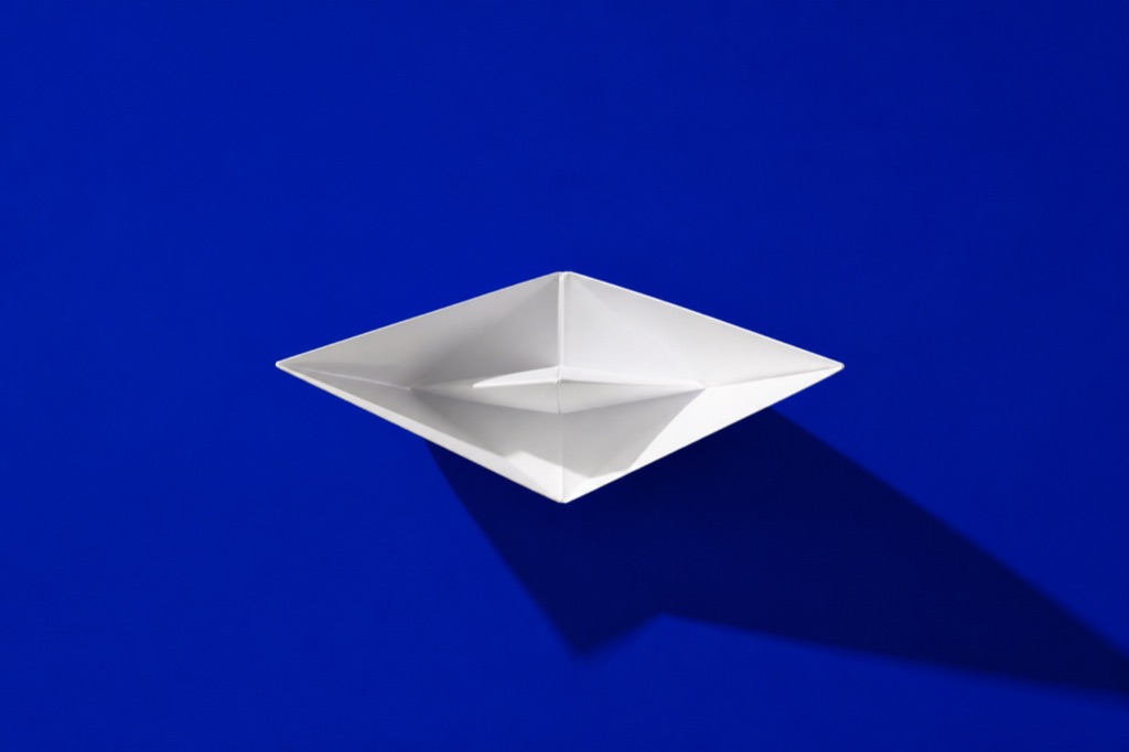Folded white paper boat on a vivid Klein-blue backdrop