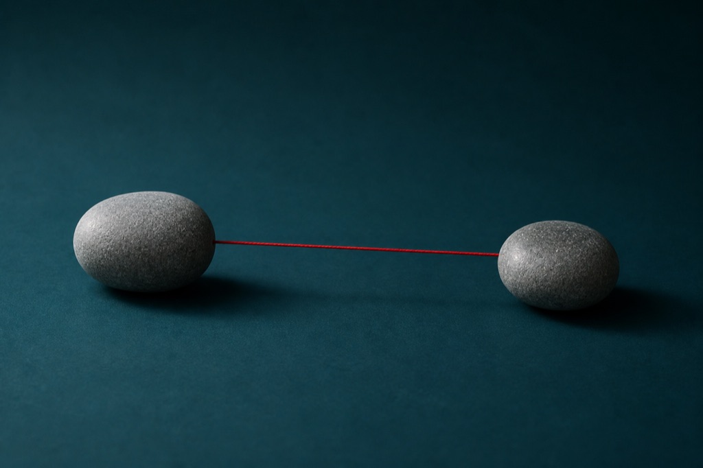 Two smooth grey river stones on a deep teal backdrop, joined by a single taut scarlet thread
